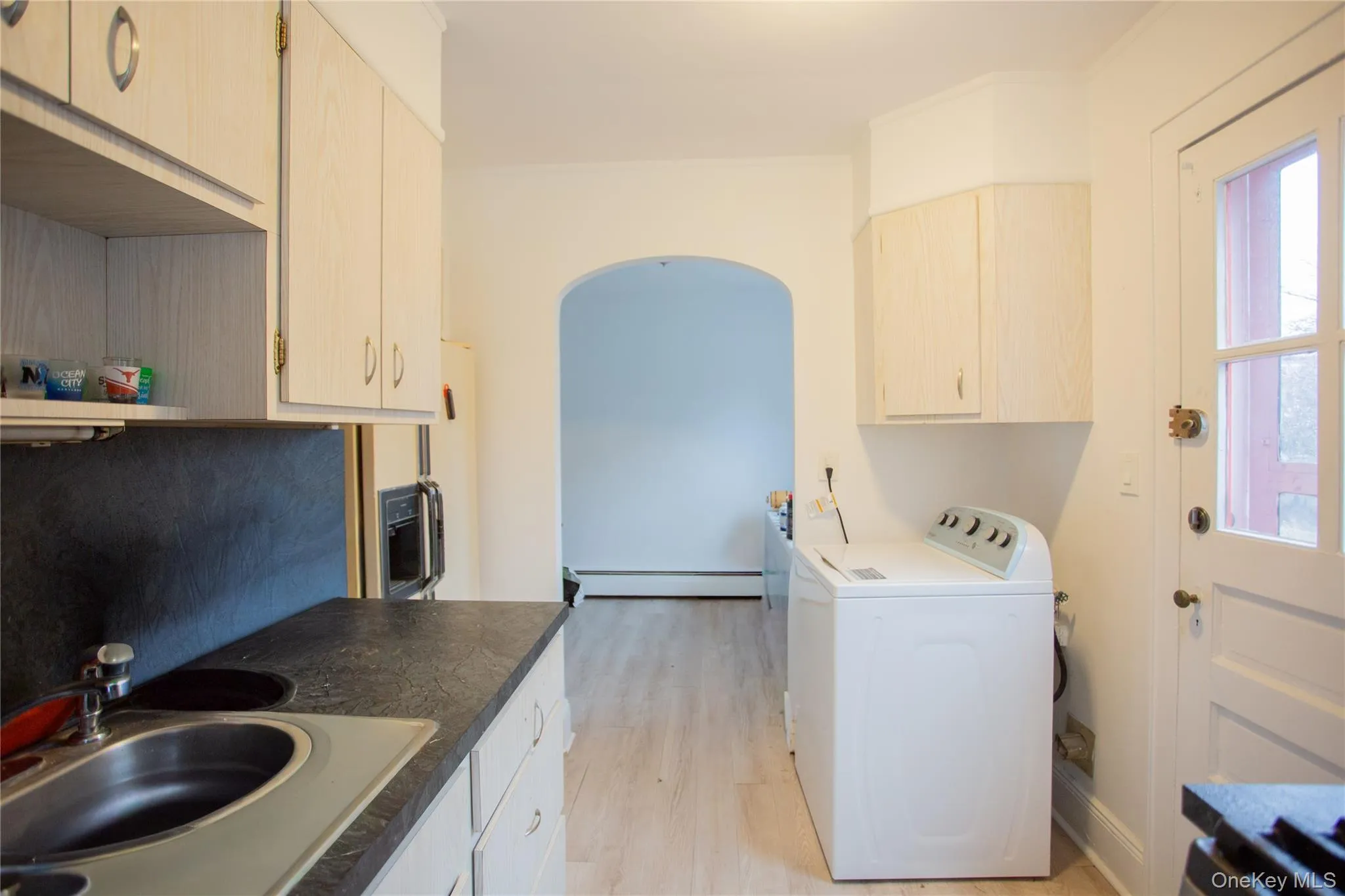 Kitchen featuring washer / clothes dryer, light wood-type flooring, baseboard heating, open shelves, and fridge with ice dispenser Kitchen featuring washer / clothes dryer, light wood-type flooring, baseboard heating, open shelves, and fridge with ice dispenser