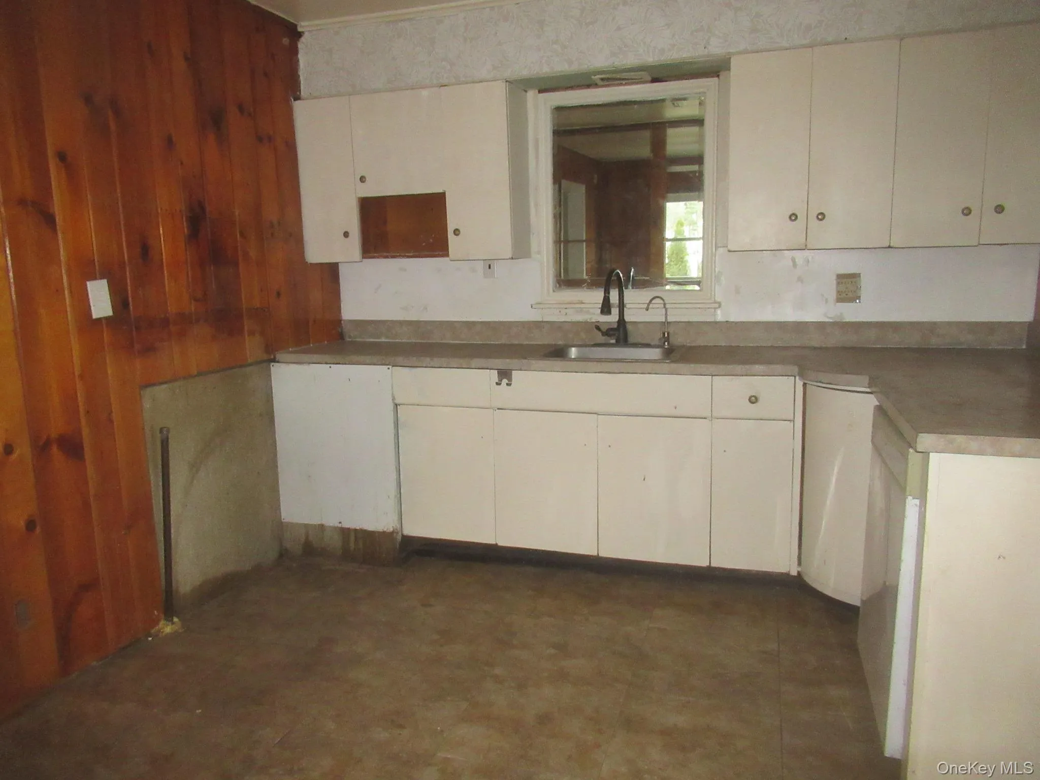 Kitchen featuring light countertops, dishwashing machine, wooden walls, cream cabinetry, and dark flooring Kitchen featuring light countertops, dishwashing machine, wooden walls, cream cabinetry, and dark flooring