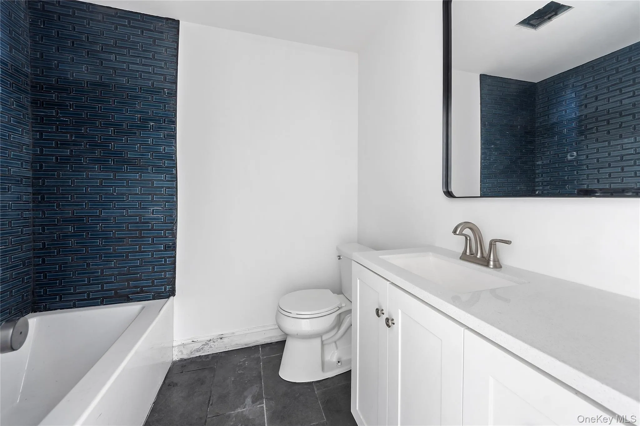 Bathroom featuring vanity, tub / shower combination, and dark tile patterned flooring Bathroom featuring vanity, tub / shower combination, and dark tile patterned flooring