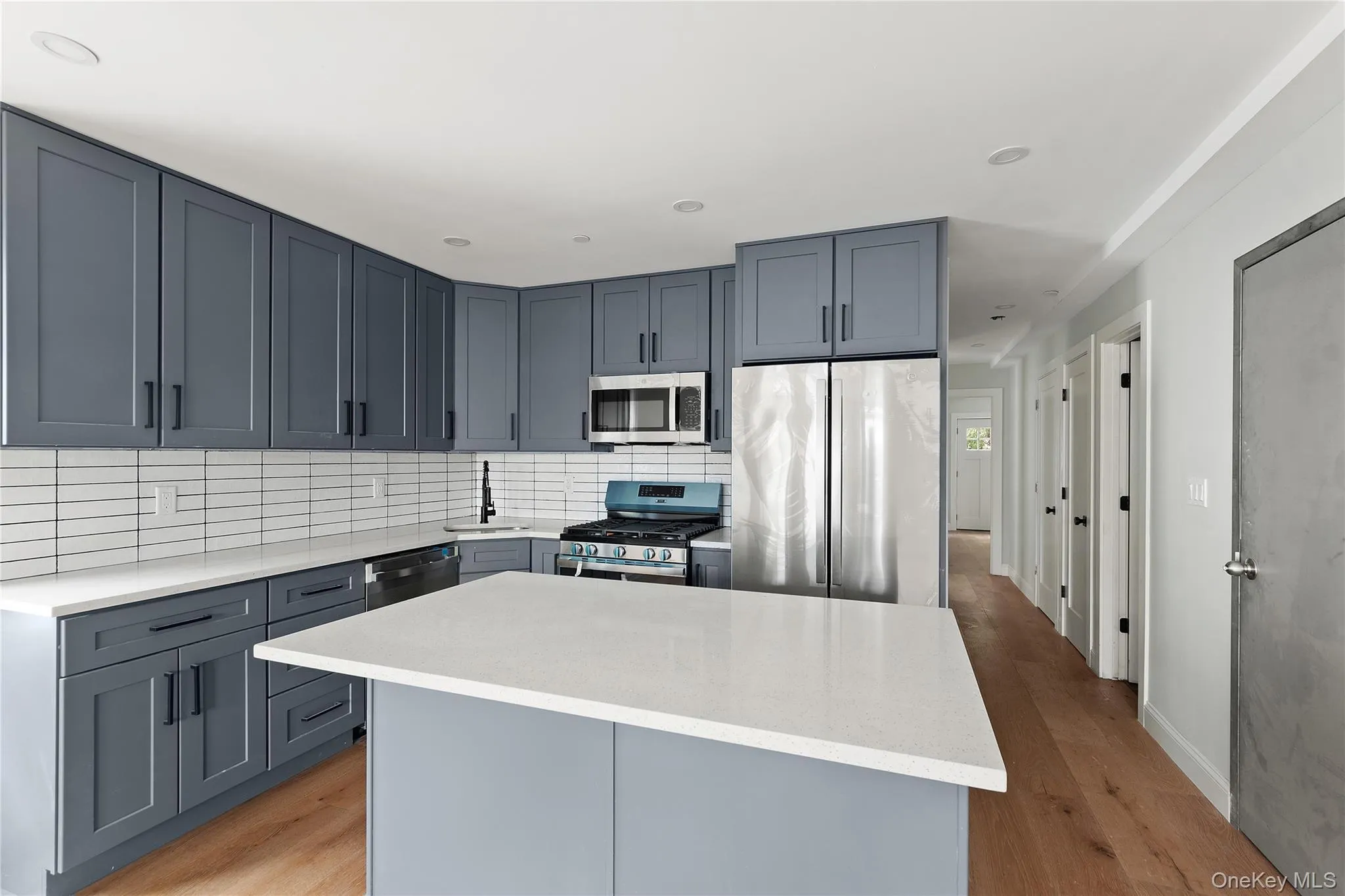 Kitchen featuring stainless steel appliances, a center island, light wood-type flooring, gray cabinetry, and tasteful backsplash Kitchen featuring stainless steel appliances, a center island, light wood-type flooring, gray cabinetry, and tasteful backsplash