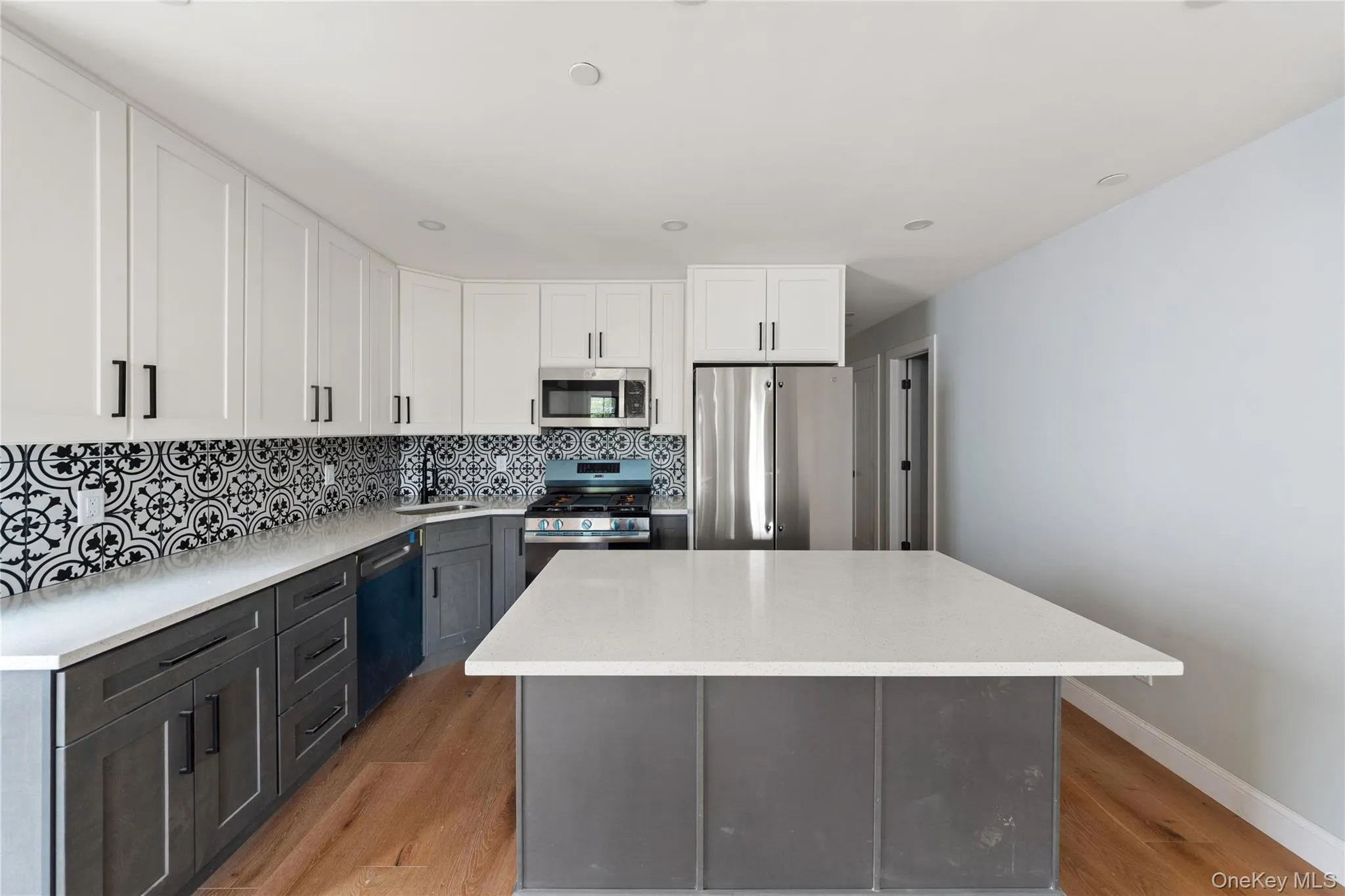 Kitchen featuring tasteful backsplash, white cabinetry, stainless steel appliances, light wood-style floors, and a kitchen island Kitchen featuring tasteful backsplash, white cabinetry, stainless steel appliances, light wood-style floors, and a kitchen island