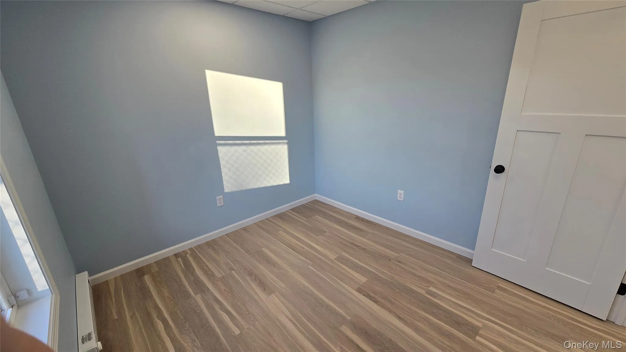 Room featuring baseboard heating, wood finished floors, and a paneled ceiling Room featuring baseboard heating, wood finished floors, and a paneled ceiling