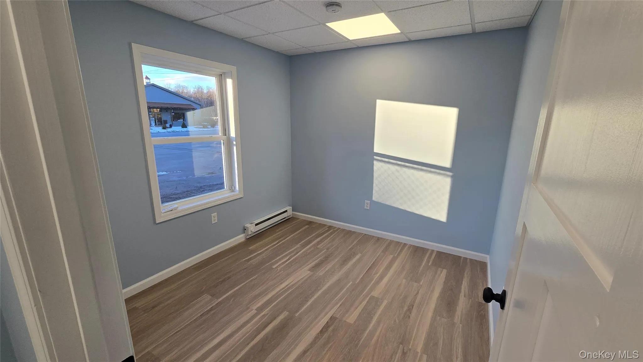 Room featuring baseboard heating, wood finished floors, and a paneled ceiling Room featuring baseboard heating, wood finished floors, and a paneled ceiling