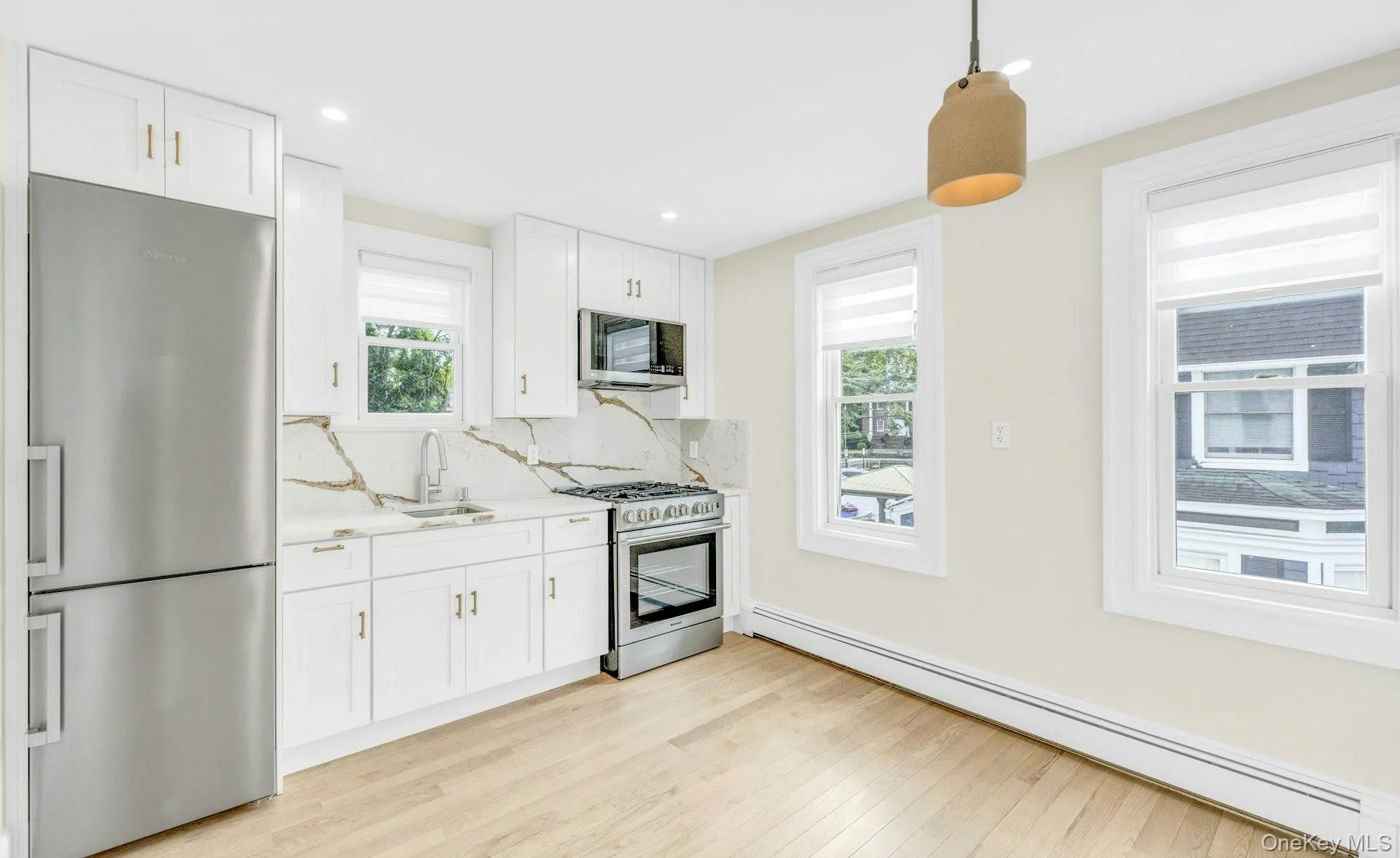 Kitchen with high end appliances with stainless steel finishes, a baseboard heating unit, hanging light fixtures, decorative backsplash, and white cabinets Kitchen with high end appliances with stainless steel finishes, a baseboard heating unit, hanging light fixtures, decorative backsplash, and white cabinets