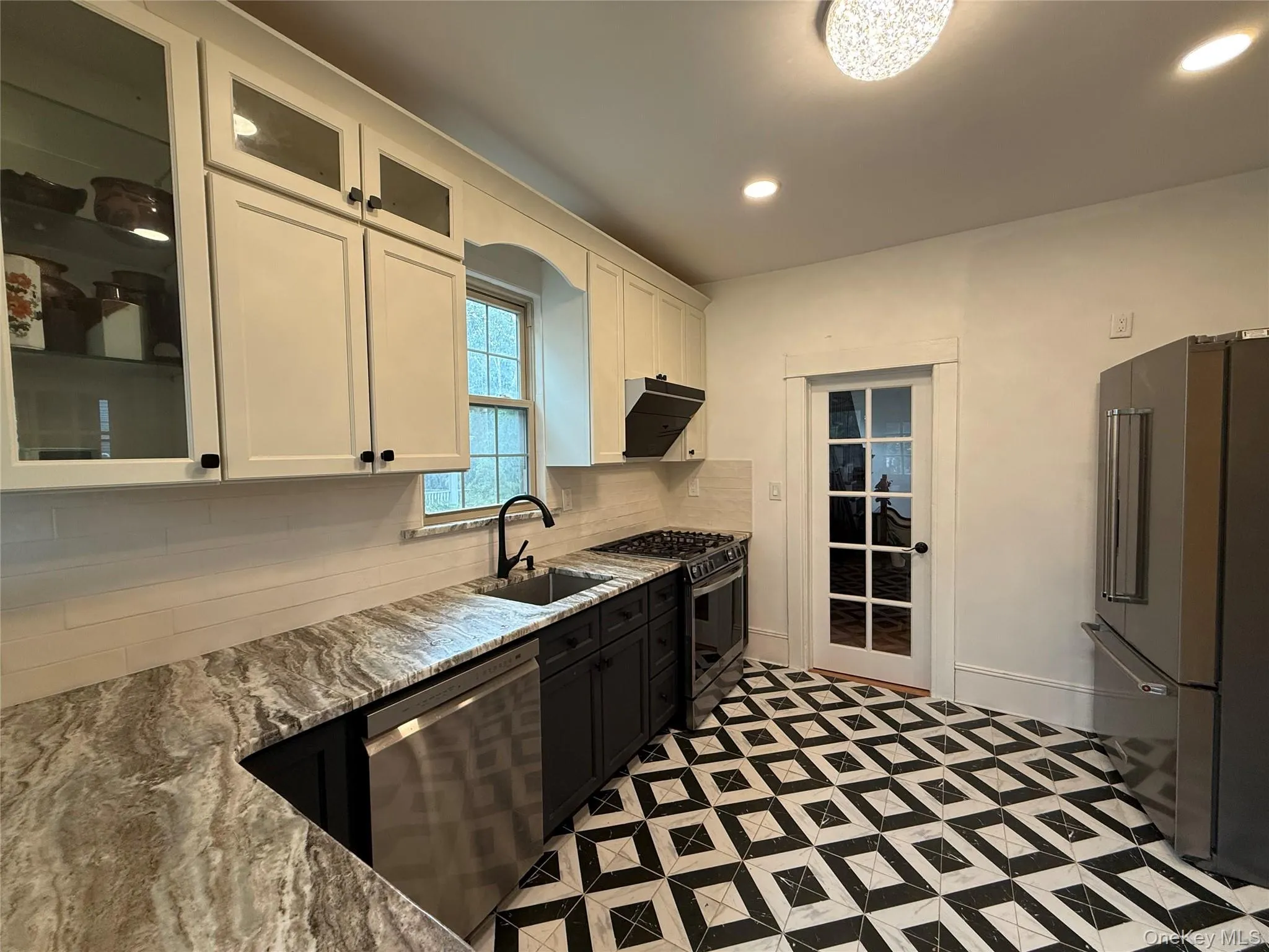 Kitchen with white cabinetry, glass insert cabinets, light stone countertops, appliances with stainless steel finishes, and recessed lighting Kitchen with white cabinetry, glass insert cabinets, light stone countertops, appliances with stainless steel finishes, and recessed lighting
