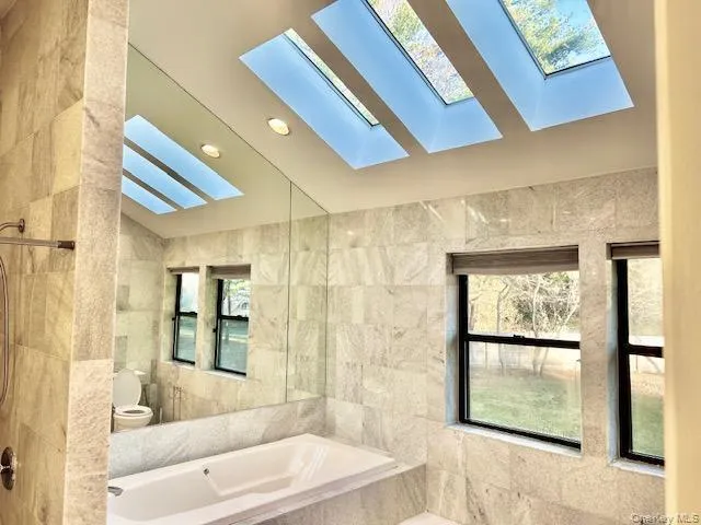 Full bath with tile walls, vaulted ceiling, a garden tub, and a skylight Full bath with tile walls, vaulted ceiling, a garden tub, and a skylight