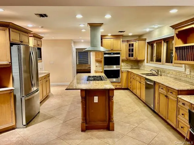 Kitchen with light stone counters, a center island, appliances with stainless steel finishes, tasteful backsplash, and brown cabinets Kitchen with light stone counters, a center island, appliances with stainless steel finishes, tasteful backsplash, and brown cabinets