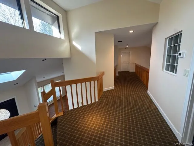 Hall with recessed lighting, vaulted ceiling, dark carpet, a skylight, and an upstairs landing Hall with recessed lighting, vaulted ceiling, dark carpet, a skylight, and an upstairs landing