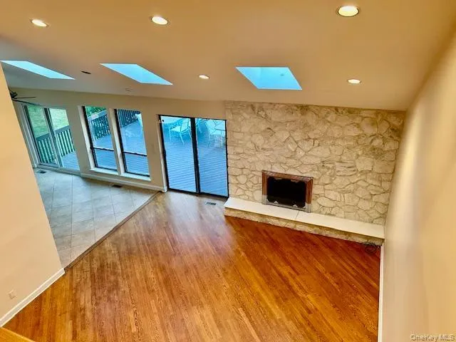 Unfurnished living room featuring light wood-style flooring, healthy amount of natural light, recessed lighting, a fireplace, and a skylight Unfurnished living room featuring light wood-style flooring, healthy amount of natural light, recessed lighting, a fireplace, and a skylight
