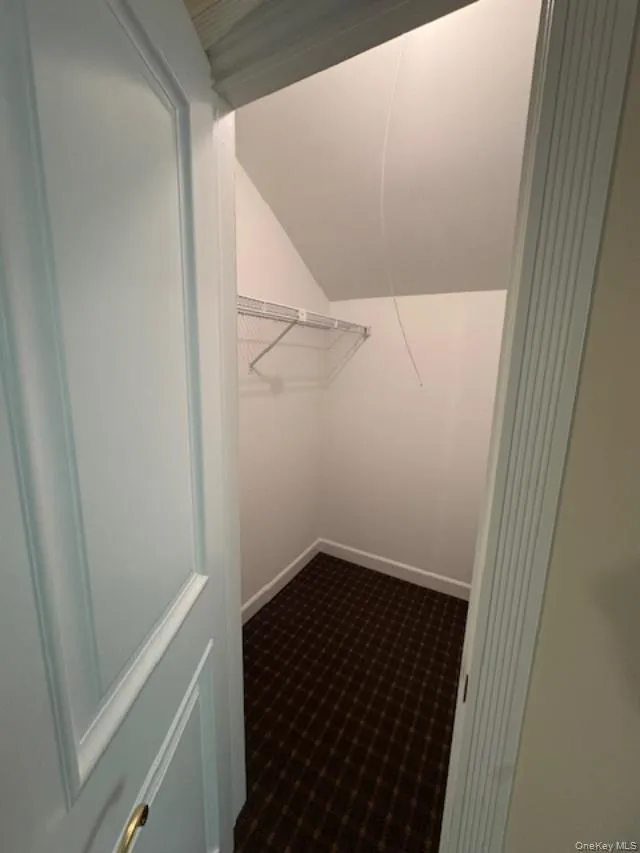 Walk in closet featuring lofted ceiling and dark colored carpet Walk in closet featuring lofted ceiling and dark colored carpet