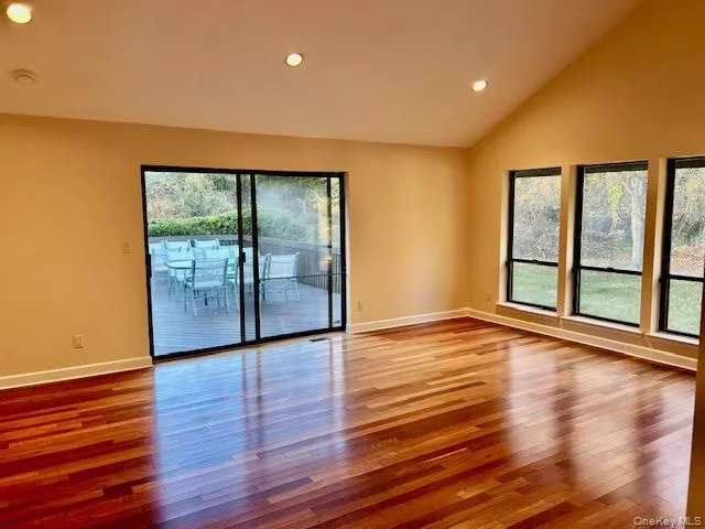 Empty room with wood finished floors, plenty of natural light, recessed lighting, and high vaulted ceiling Empty room with wood finished floors, plenty of natural light, recessed lighting, and high vaulted ceiling