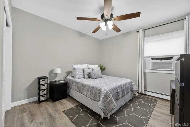 Bedroom featuring a ceiling fan, light wood-style floors, cooling unit, a baseboard radiator, and a closet Bedroom featuring a ceiling fan, light wood-style floors, cooling unit, a baseboard radiator, and a closet