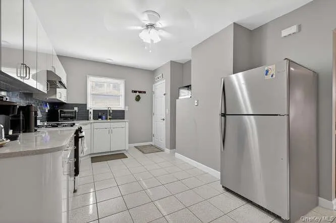 Kitchen with appliances with stainless steel finishes, white cabinets, light tile patterned flooring, and tasteful backsplash Kitchen with appliances with stainless steel finishes, white cabinets, light tile patterned flooring, and tasteful backsplash
