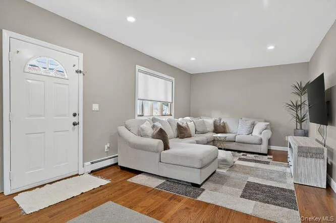 Living room featuring wood finished floors, a baseboard heating unit, and recessed lighting Living room featuring wood finished floors, a baseboard heating unit, and recessed lighting