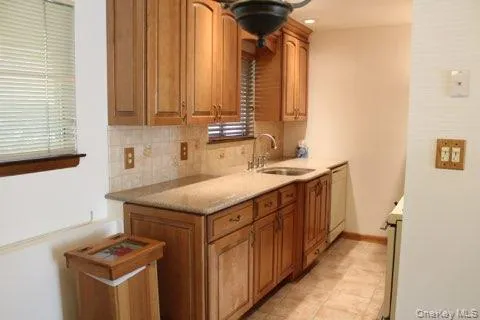 Kitchen featuring backsplash, brown cabinets, stainless steel stove, and white dishwasher Kitchen featuring backsplash, brown cabinets, stainless steel stove, and white dishwasher