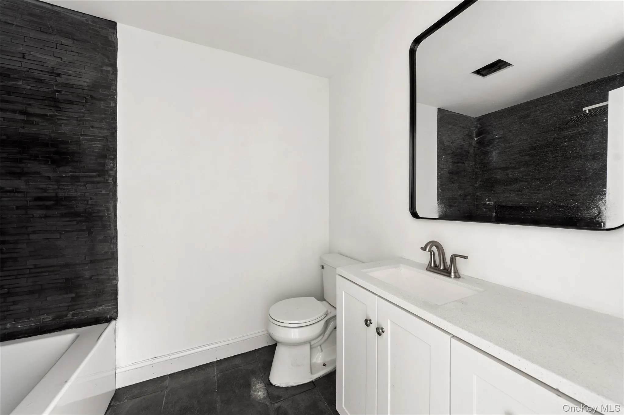 Full bathroom with vanity, dark tile patterned flooring, and washtub / shower combination Full bathroom with vanity, dark tile patterned flooring, and washtub / shower combination
