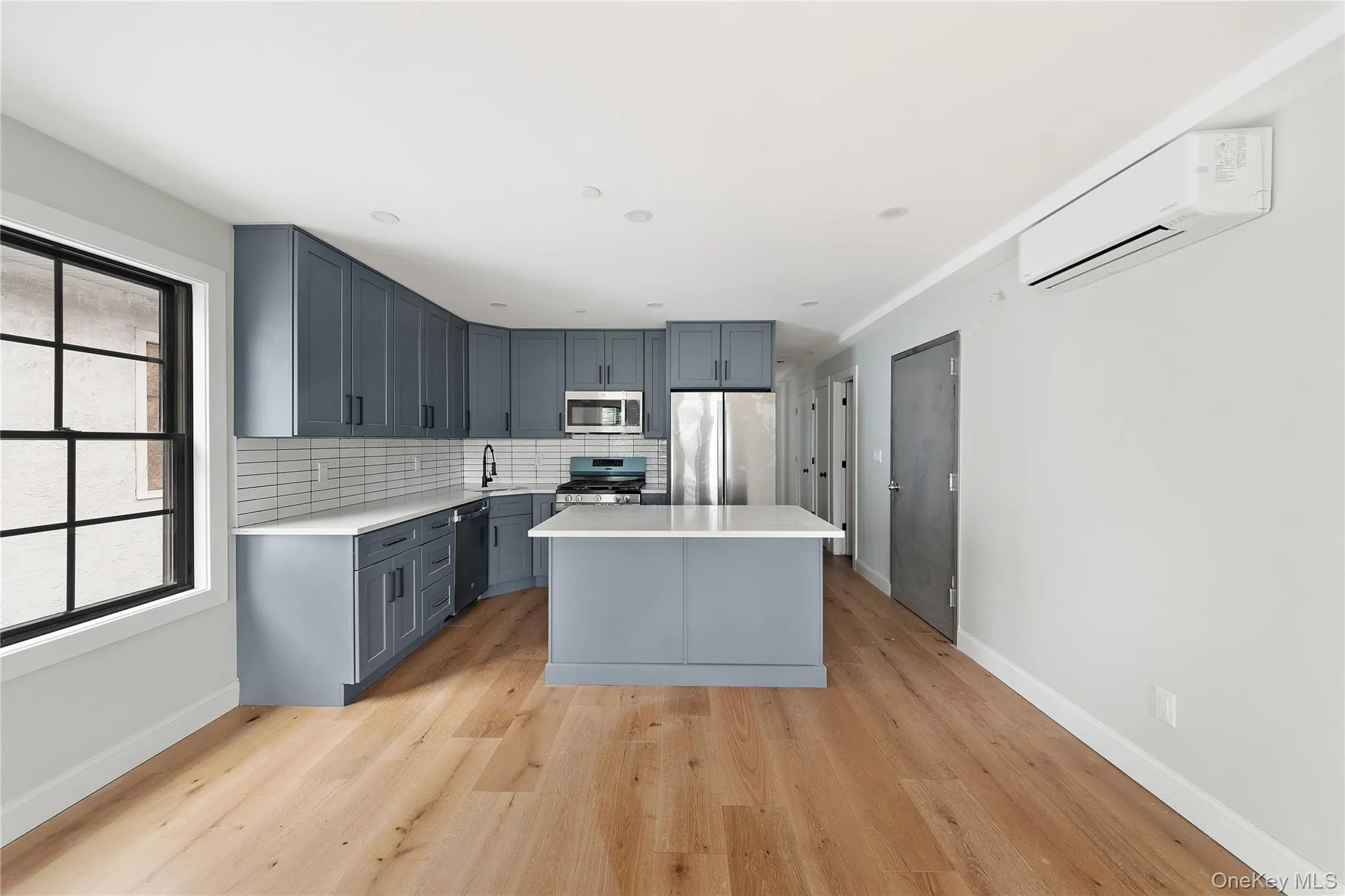Kitchen with a center island, decorative backsplash, light wood-style flooring, gray cabinets, and appliances with stainless steel finishes Kitchen with a center island, decorative backsplash, light wood-style flooring, gray cabinets, and appliances with stainless steel finishes
