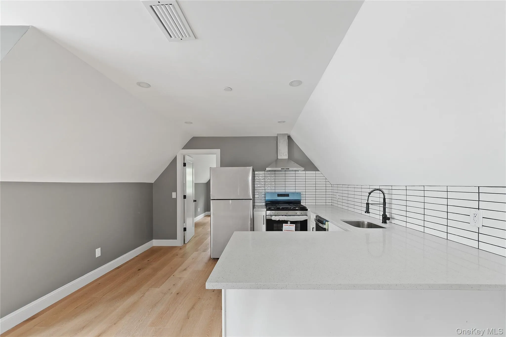 Kitchen featuring light stone counters, stainless steel appliances, a peninsula, wall chimney range hood, and lofted ceiling Kitchen featuring light stone counters, stainless steel appliances, a peninsula, wall chimney range hood, and lofted ceiling