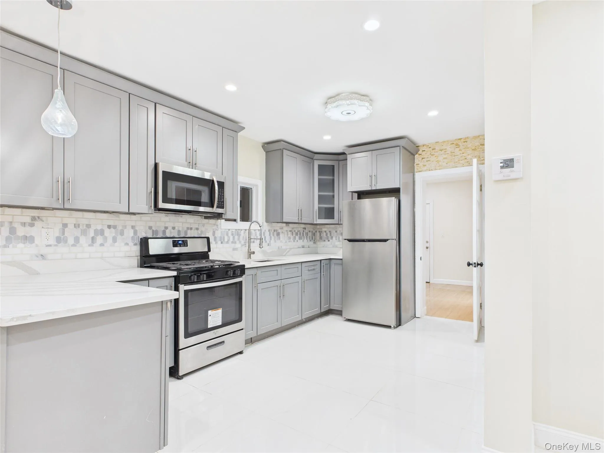 Kitchen featuring gray cabinets, appliances with stainless steel finishes, decorative light fixtures, glass insert cabinets, and recessed lighting Kitchen featuring gray cabinets, appliances with stainless steel finishes, decorative light fixtures, glass insert cabinets, and recessed lighting