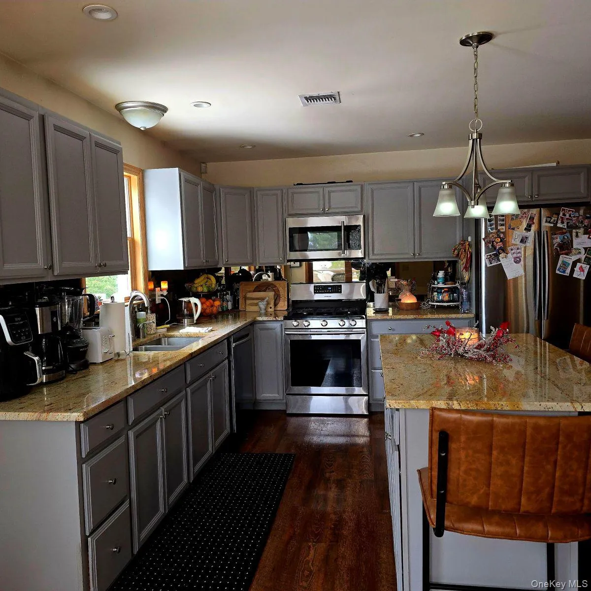 Kitchen featuring gray cabinetry, light stone counters, pendant lighting, appliances with stainless steel finishes, and dark wood-type flooring Kitchen featuring gray cabinetry, light stone counters, pendant lighting, appliances with stainless steel finishes, and dark wood-type flooring