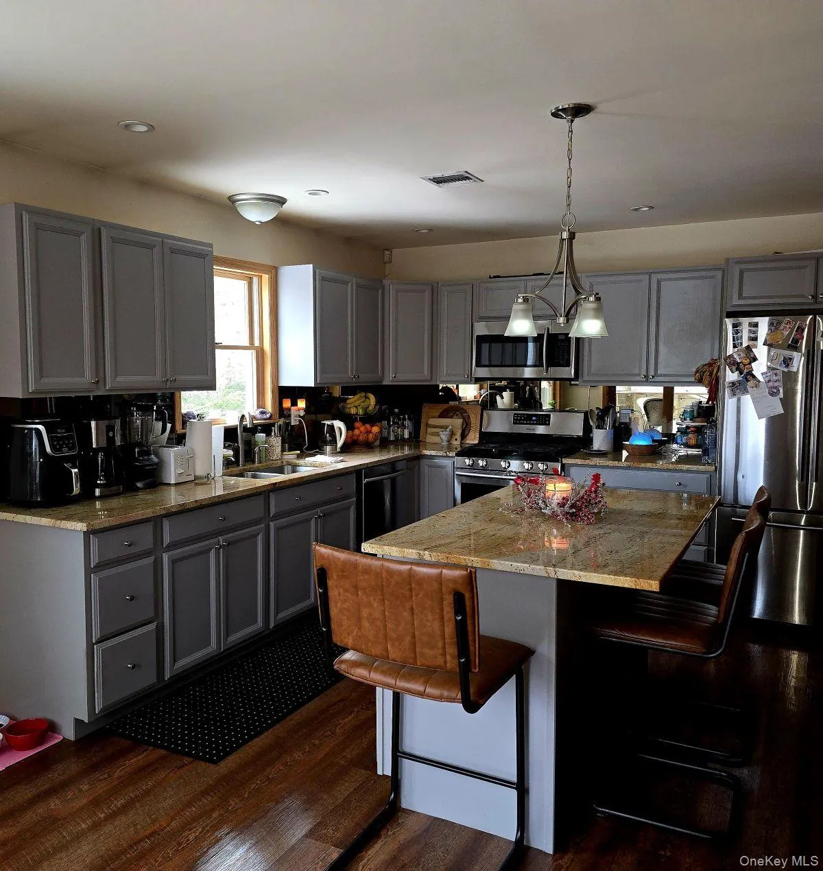 Kitchen with gray cabinets, a kitchen breakfast bar, hanging light fixtures, and appliances with stainless steel finishes Kitchen with gray cabinets, a kitchen breakfast bar, hanging light fixtures, and appliances with stainless steel finishes
