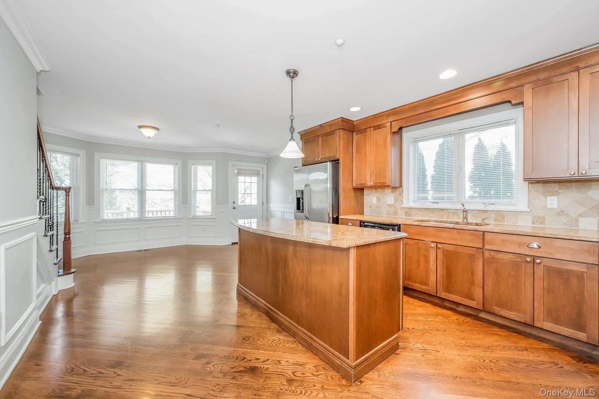Kitchen featuring brown cabinets, light stone countertops, plenty of natural light, crown molding, and a decorative wall Kitchen featuring brown cabinets, light stone countertops, plenty of natural light, crown molding, and a decorative wall