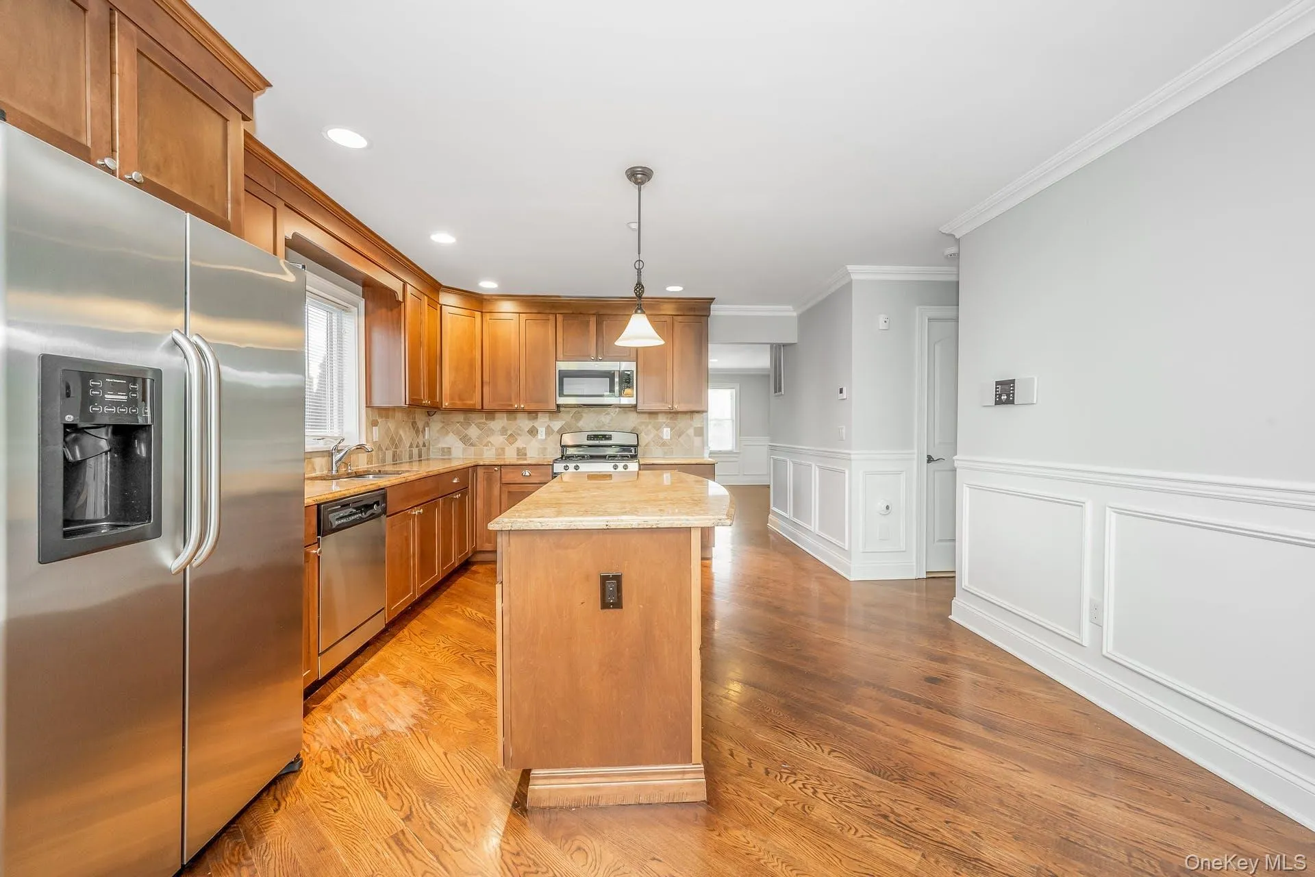 Kitchen with stainless steel appliances, light stone counters, a center island, brown cabinetry, and light wood finished floors Kitchen with stainless steel appliances, light stone counters, a center island, brown cabinetry, and light wood finished floors