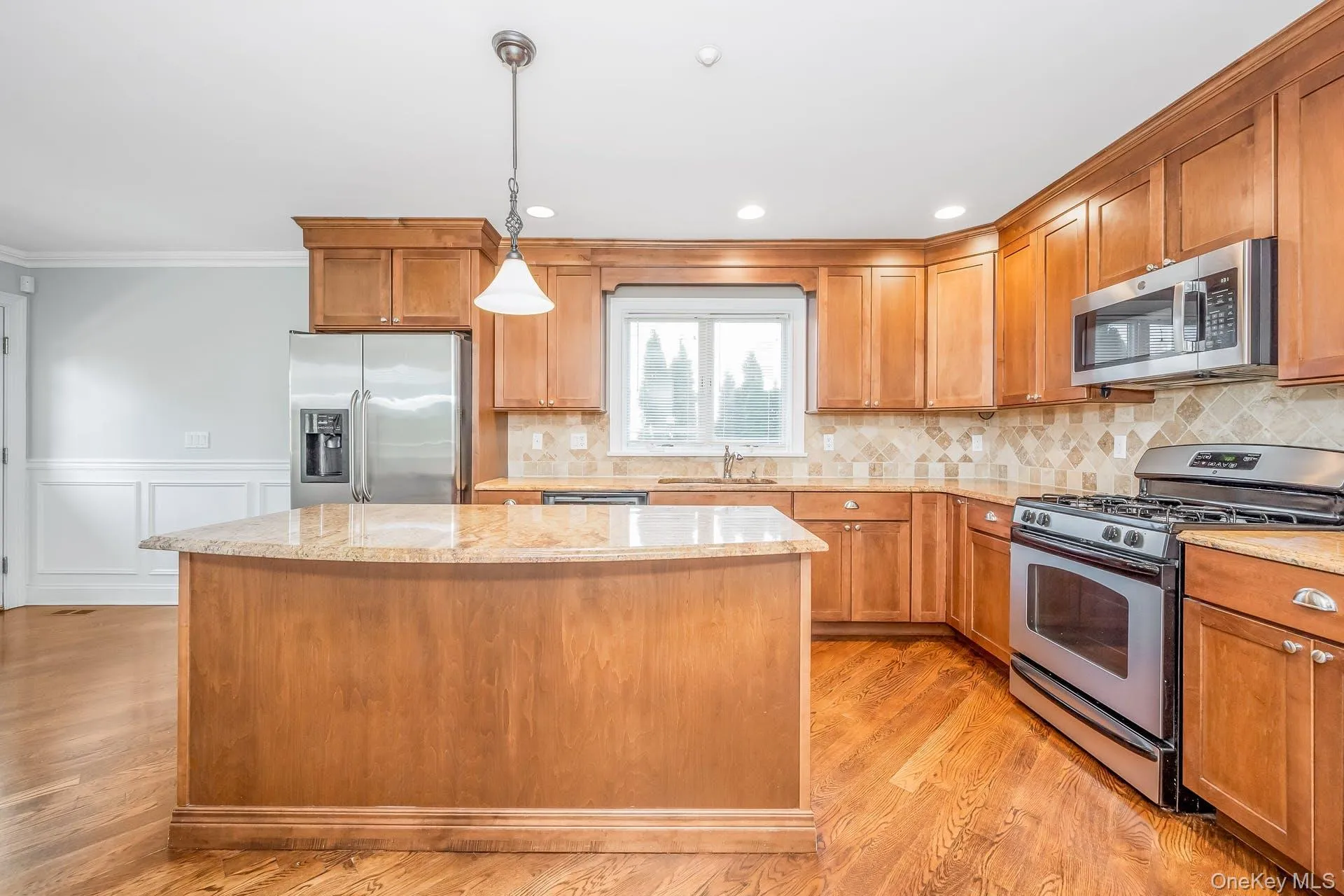 Kitchen featuring appliances with stainless steel finishes, brown cabinets, decorative light fixtures, backsplash, and light stone countertops Kitchen featuring appliances with stainless steel finishes, brown cabinets, decorative light fixtures, backsplash, and light stone countertops