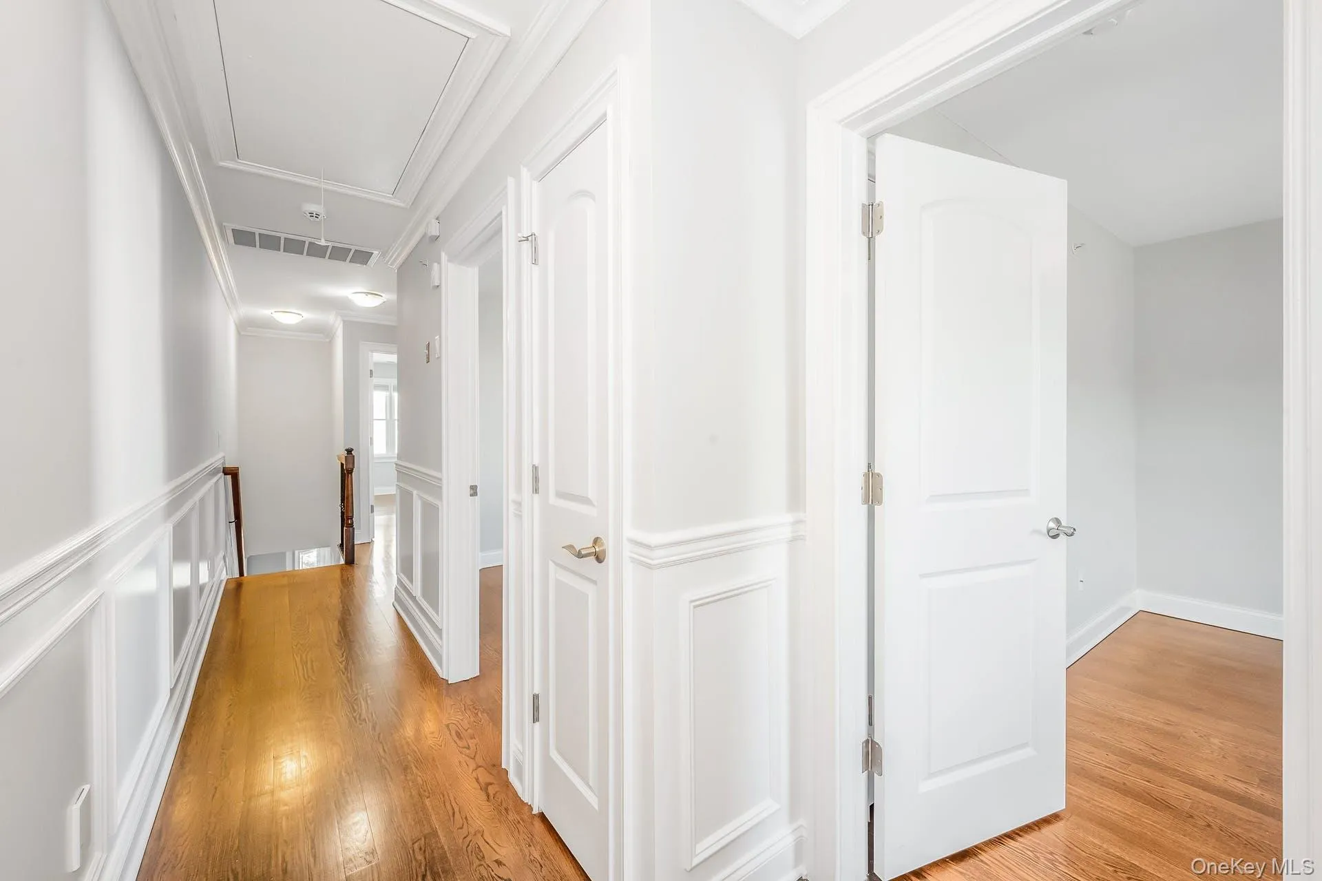 Corridor featuring attic access, light wood-style flooring, a decorative wall, and ornamental molding Corridor featuring attic access, light wood-style flooring, a decorative wall, and ornamental molding