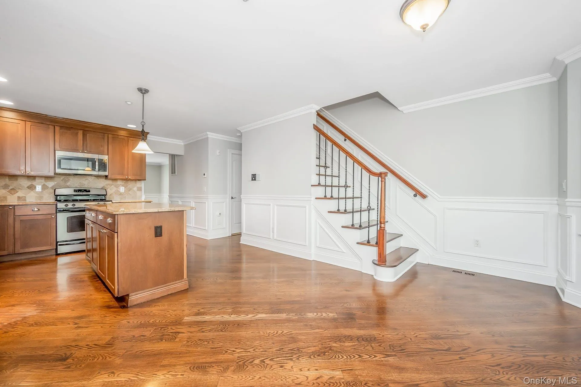 Kitchen featuring stainless steel appliances, a center island, light stone countertops, brown cabinets, and hanging light fixtures Kitchen featuring stainless steel appliances, a center island, light stone countertops, brown cabinets, and hanging light fixtures
