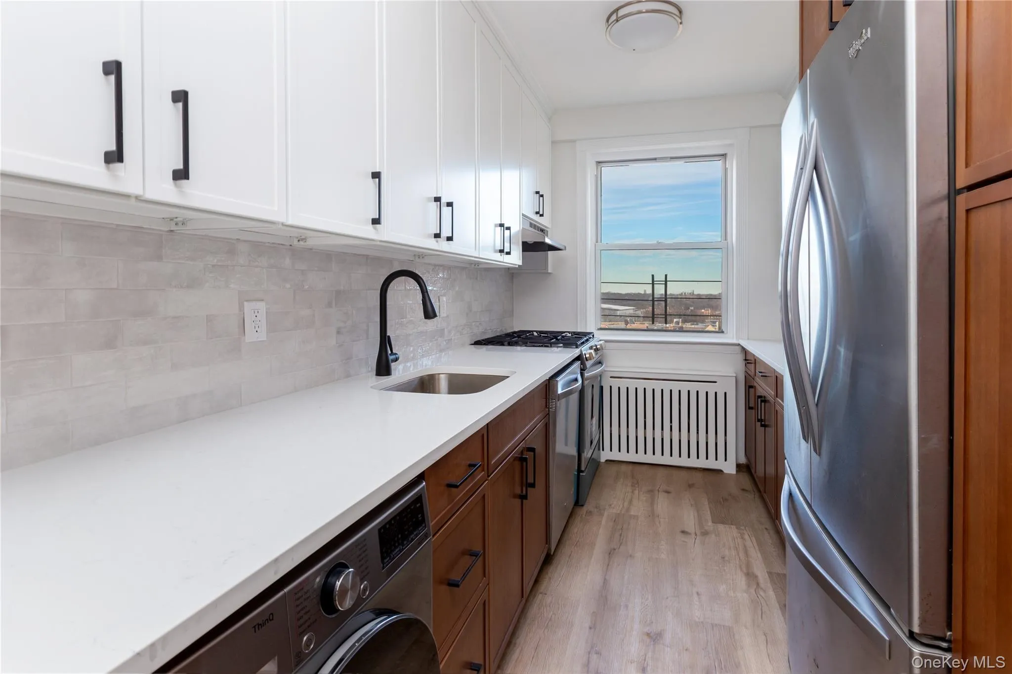 Kitchen with appliances with stainless steel finishes, washer / dryer, light wood-style flooring, light stone countertops, and backsplash Kitchen with appliances with stainless steel finishes, washer / dryer, light wood-style flooring, light stone countertops, and backsplash