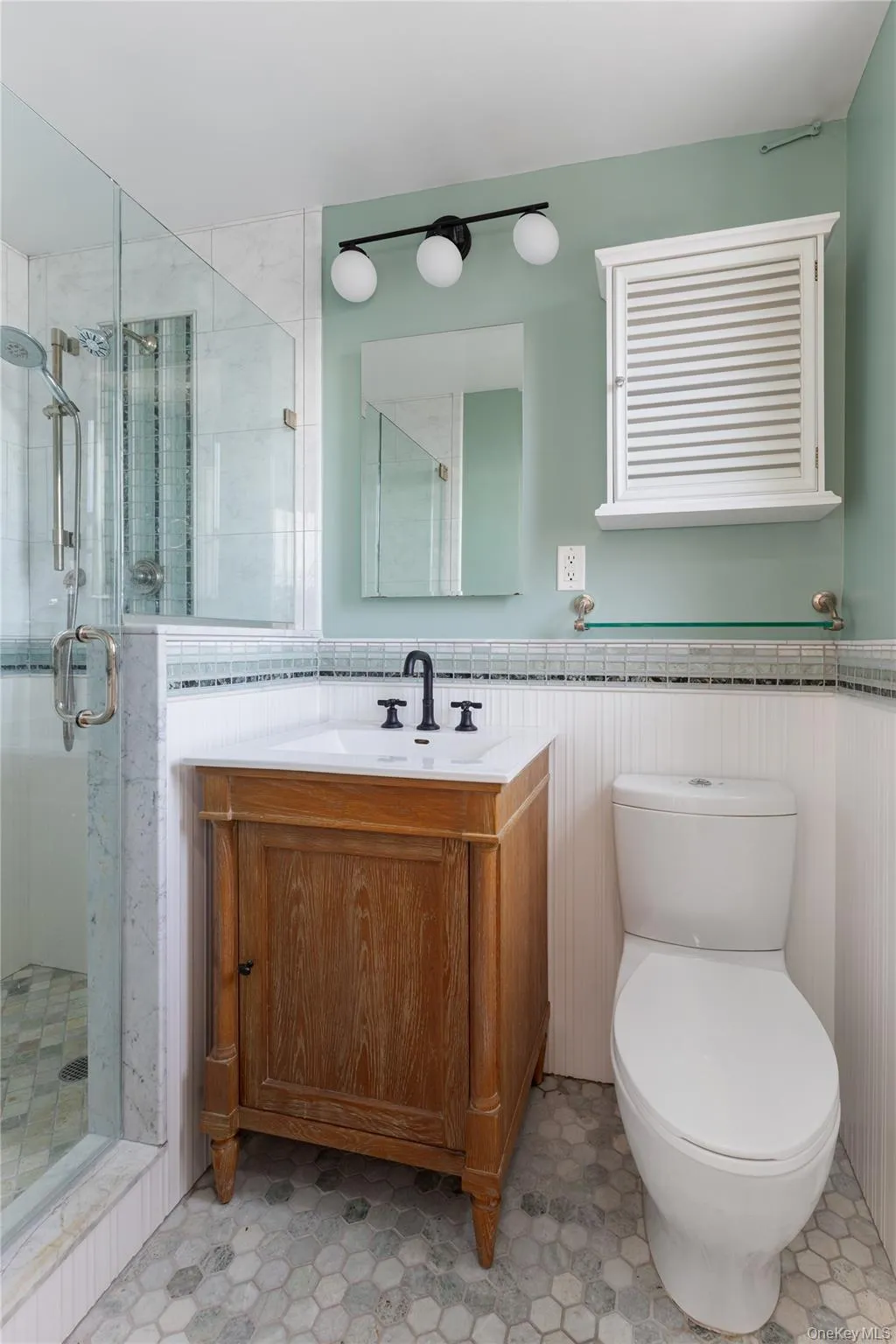 Bathroom featuring vanity, a stall shower, wainscoting, and light flooring Bathroom featuring vanity, a stall shower, wainscoting, and light flooring