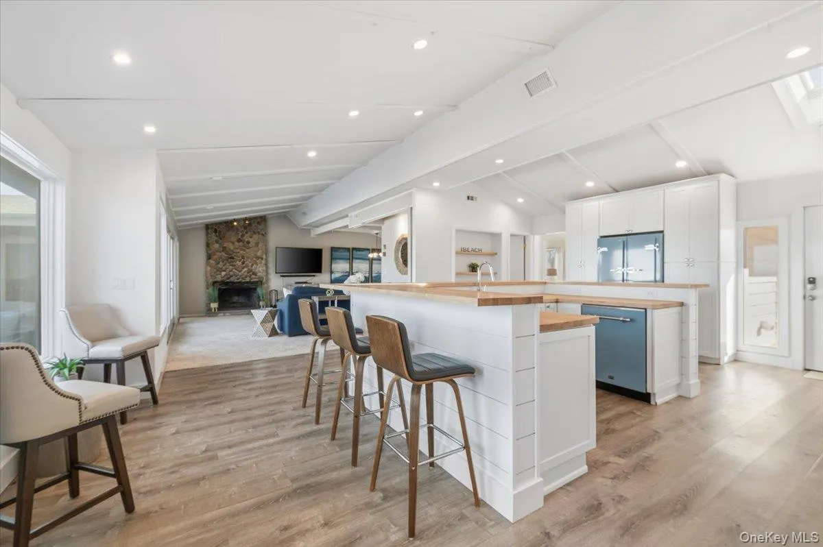 Kitchen featuring white cabinetry, a breakfast bar area, a large fireplace, dishwasher, and built in fridge Kitchen featuring white cabinetry, a breakfast bar area, a large fireplace, dishwasher, and built in fridge