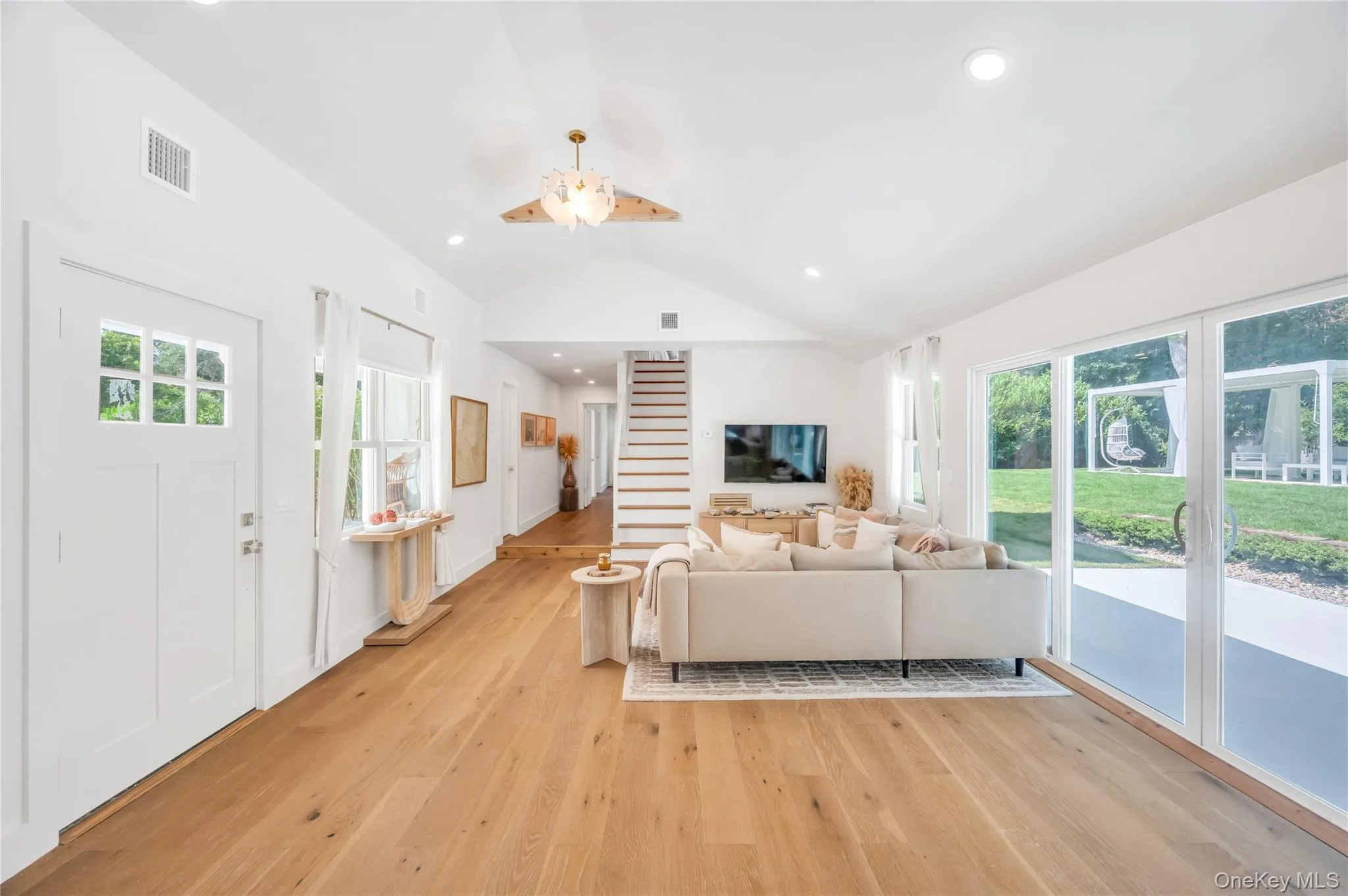 Living area featuring vaulted ceiling, light wood-style floors, healthy amount of natural light, a ceiling fan, and stairs Living area featuring vaulted ceiling, light wood-style floors, healthy amount of natural light, a ceiling fan, and stairs