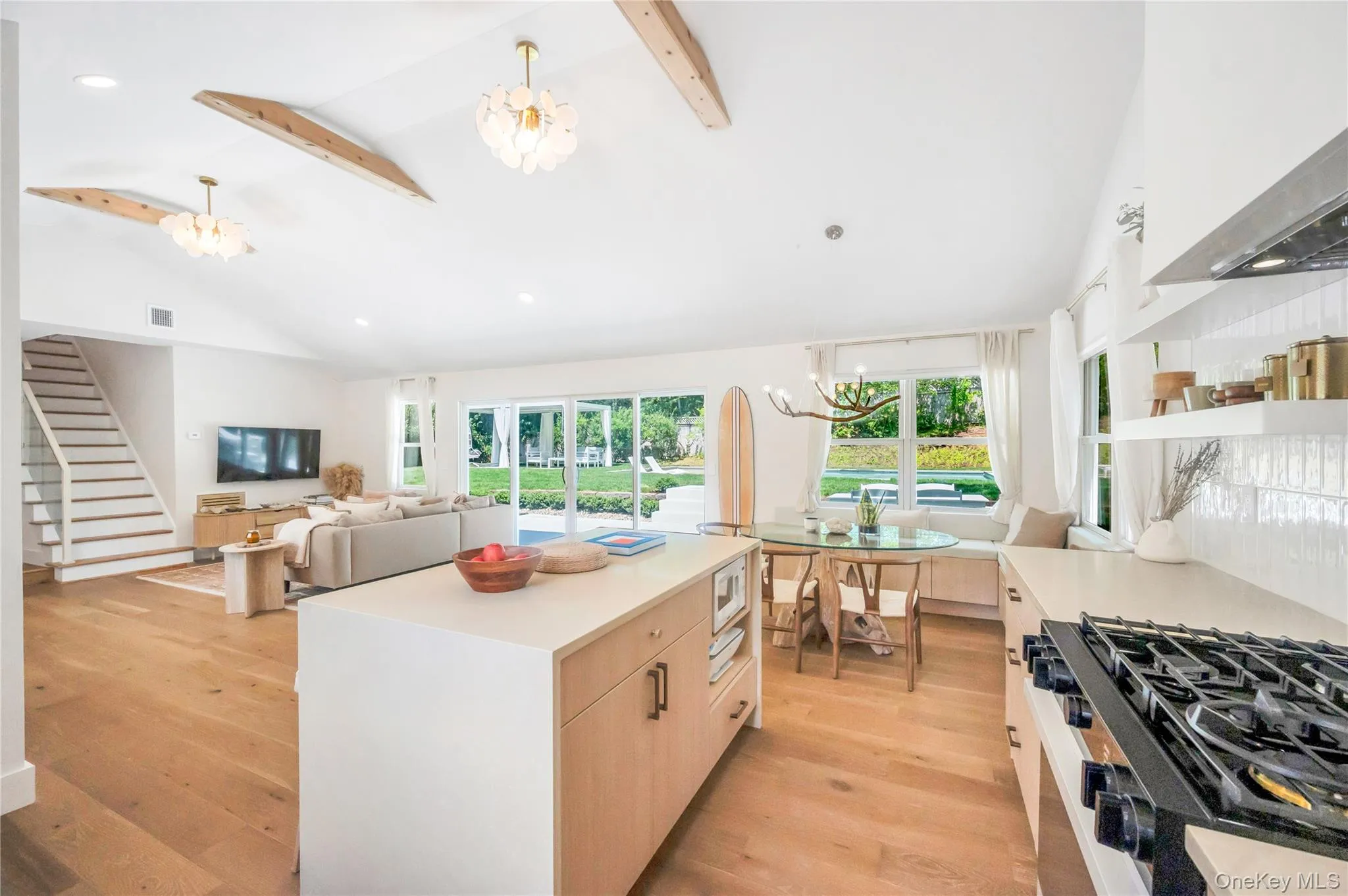 Kitchen featuring a chandelier, beam ceiling, black gas range, open floor plan, and light brown cabinets Kitchen featuring a chandelier, beam ceiling, black gas range, open floor plan, and light brown cabinets