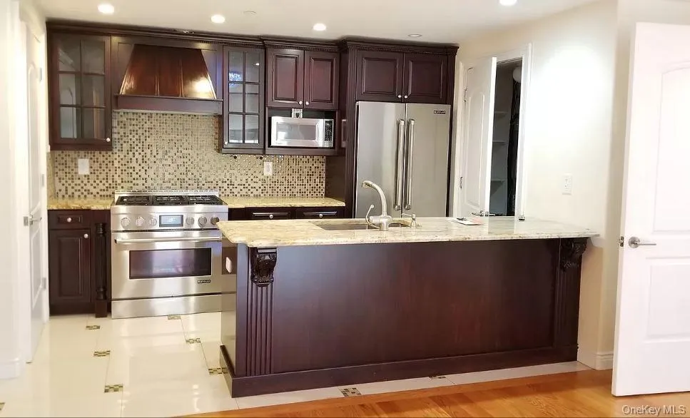 Kitchen with premium appliances, custom range hood, glass insert cabinets, backsplash, and light stone countertops Kitchen with premium appliances, custom range hood, glass insert cabinets, backsplash, and light stone countertops