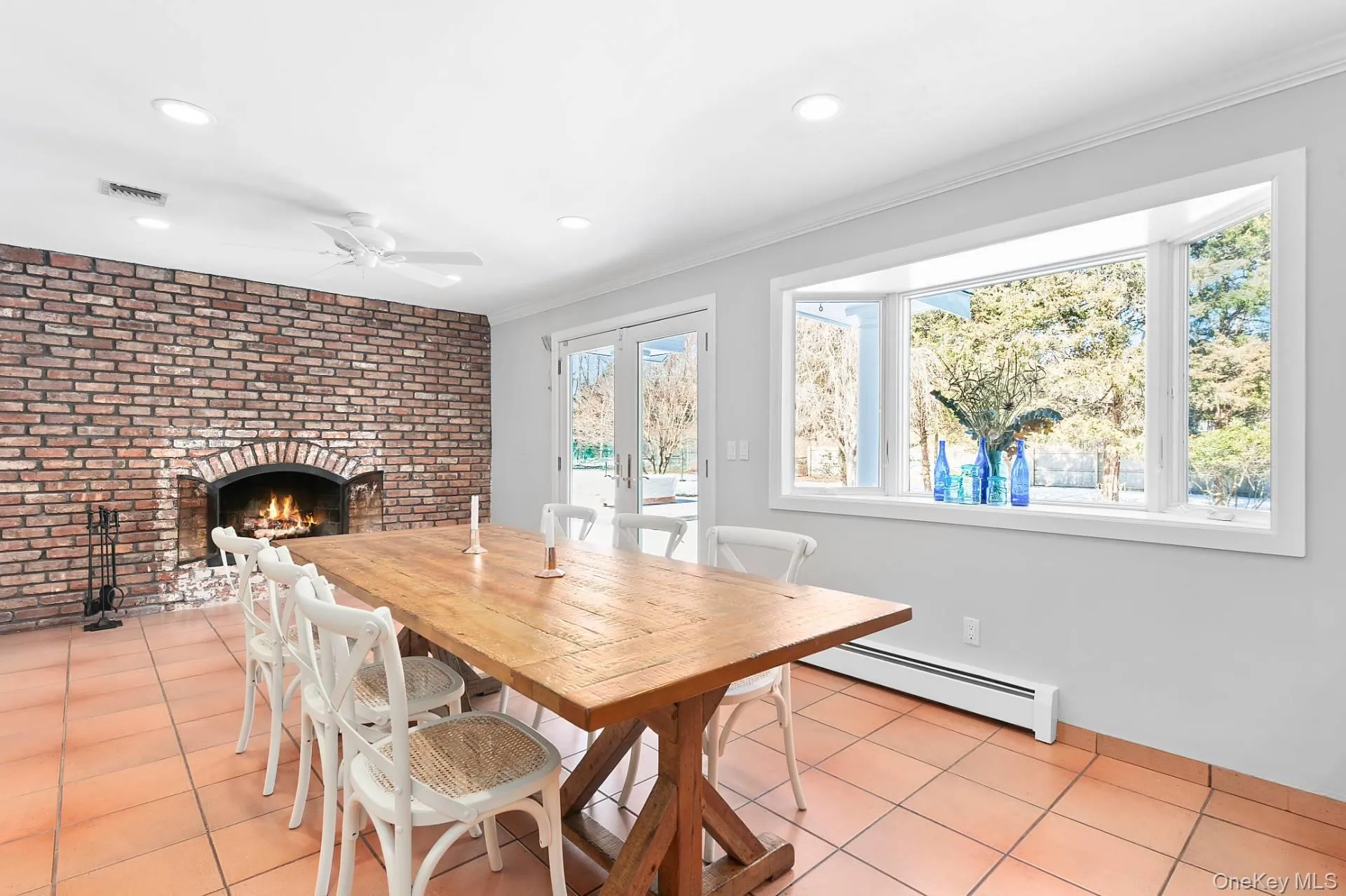 Dining area featuring french doors, baseboard heating, brick wall, light tile patterned floors, and a brick fireplace Dining area featuring french doors, baseboard heating, brick wall, light tile patterned floors, and a brick fireplace
