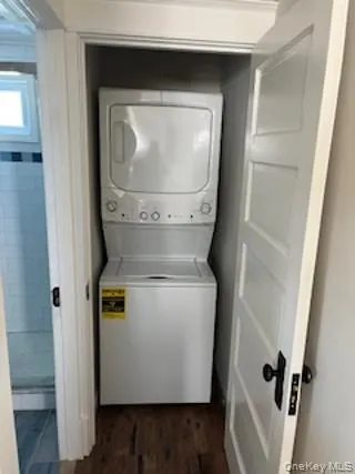 Laundry room with dark wood-style flooring and estacked washer and dryer Laundry room with dark wood-style flooring and estacked washer and dryer
