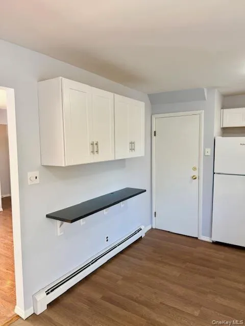 Kitchen featuring white cabinetry, baseboard heating, freestanding refrigerator, dark countertops, and dark wood-style flooring Kitchen featuring white cabinetry, baseboard heating, freestanding refrigerator, dark countertops, and dark wood-style flooring