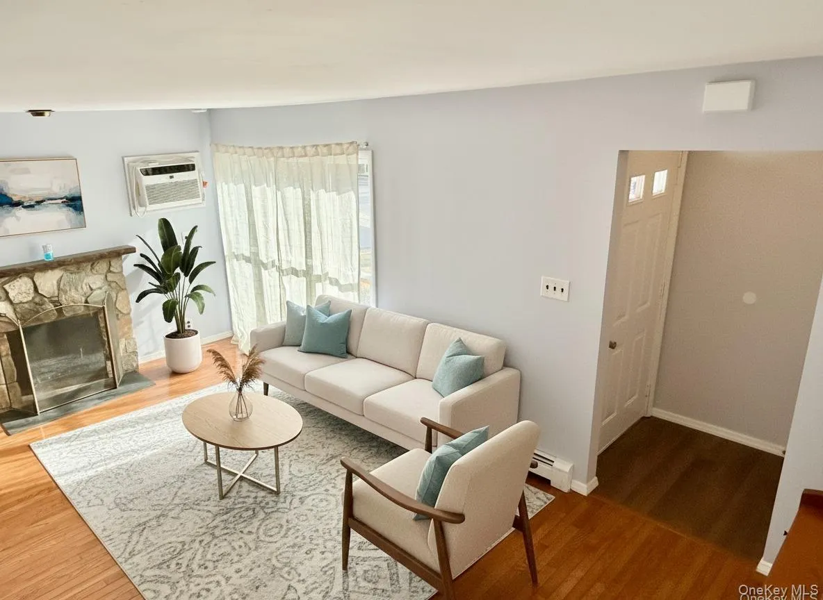 Living room featuring a stone fireplace, wood finished floors, and a baseboard radiator Living room featuring a stone fireplace, wood finished floors, and a baseboard radiator
