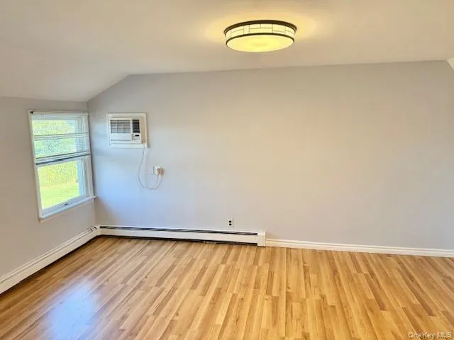 Spare room featuring lofted ceiling, light wood-style floors, a baseboard radiator, and a wall unit AC Spare room featuring lofted ceiling, light wood-style floors, a baseboard radiator, and a wall unit AC