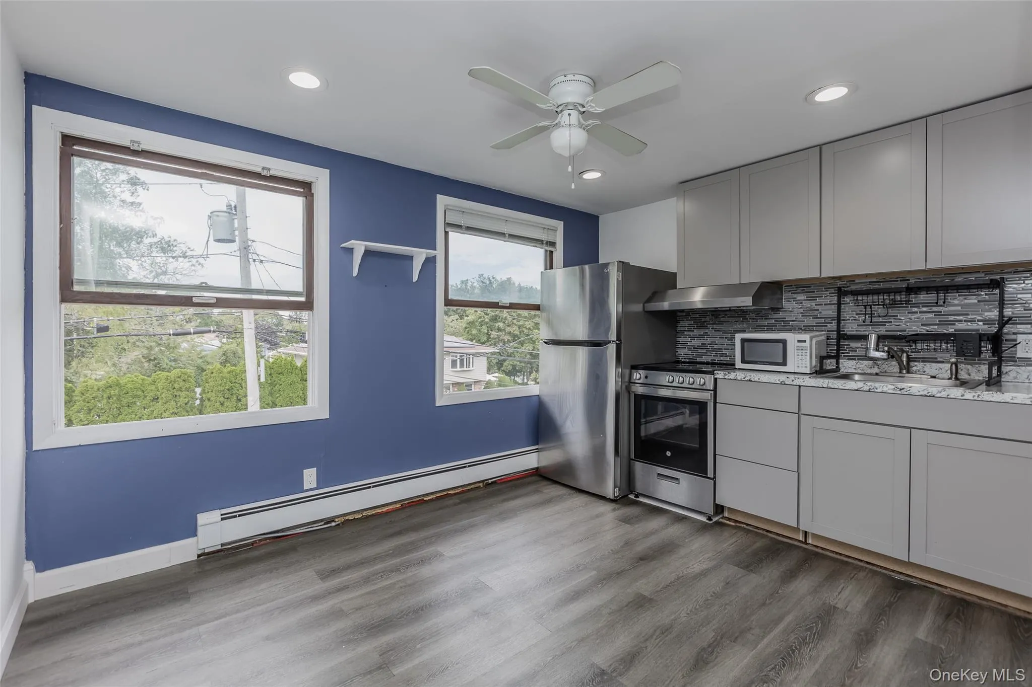 Kitchen with gray cabinets, stainless steel electric stove, baseboard heating, backsplash, and white microwave Kitchen with gray cabinets, stainless steel electric stove, baseboard heating, backsplash, and white microwave