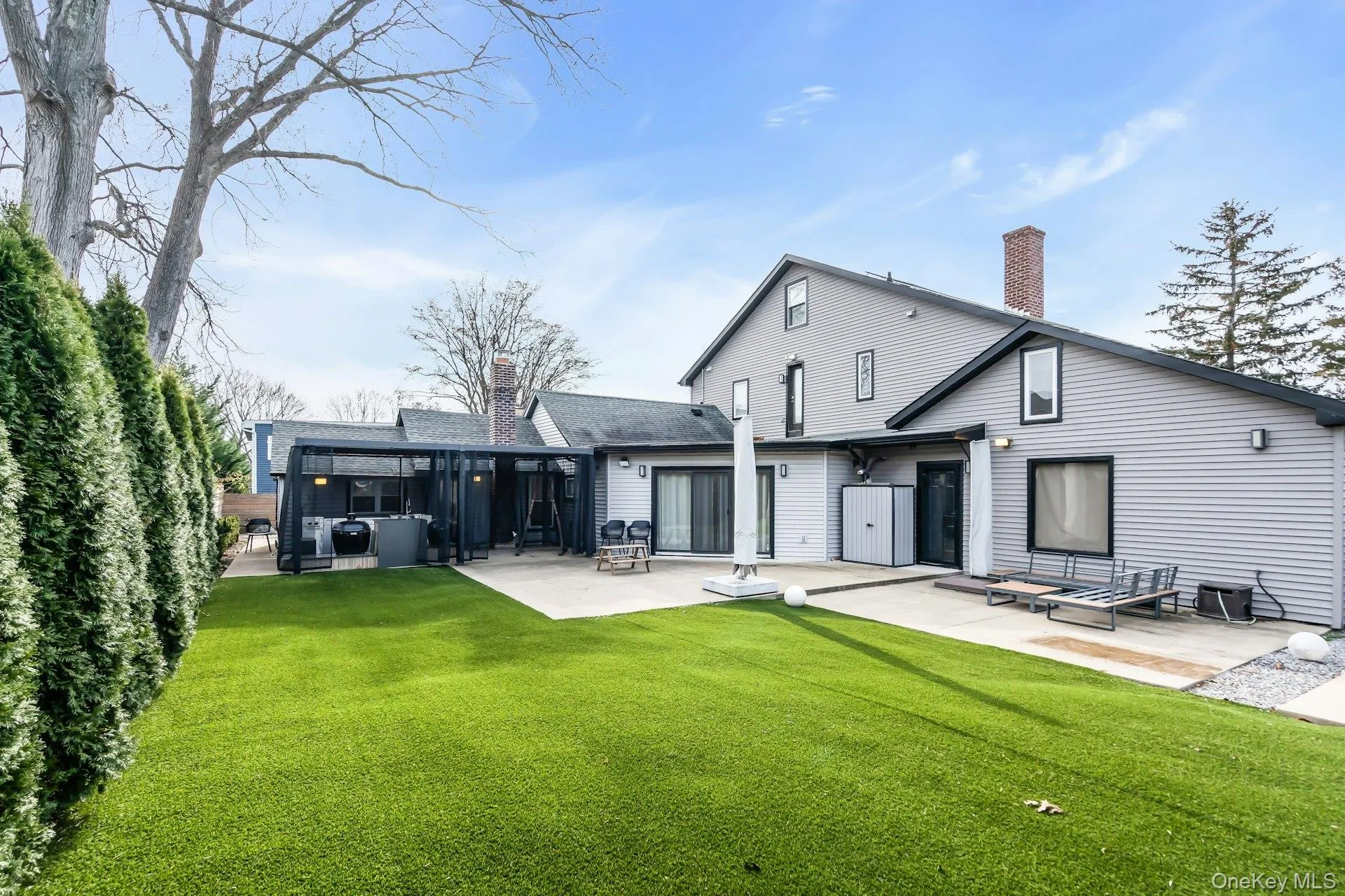 Back of house with a chimney, a patio, a lawn, and area for grilling Back of house with a chimney, a patio, a lawn, and area for grilling