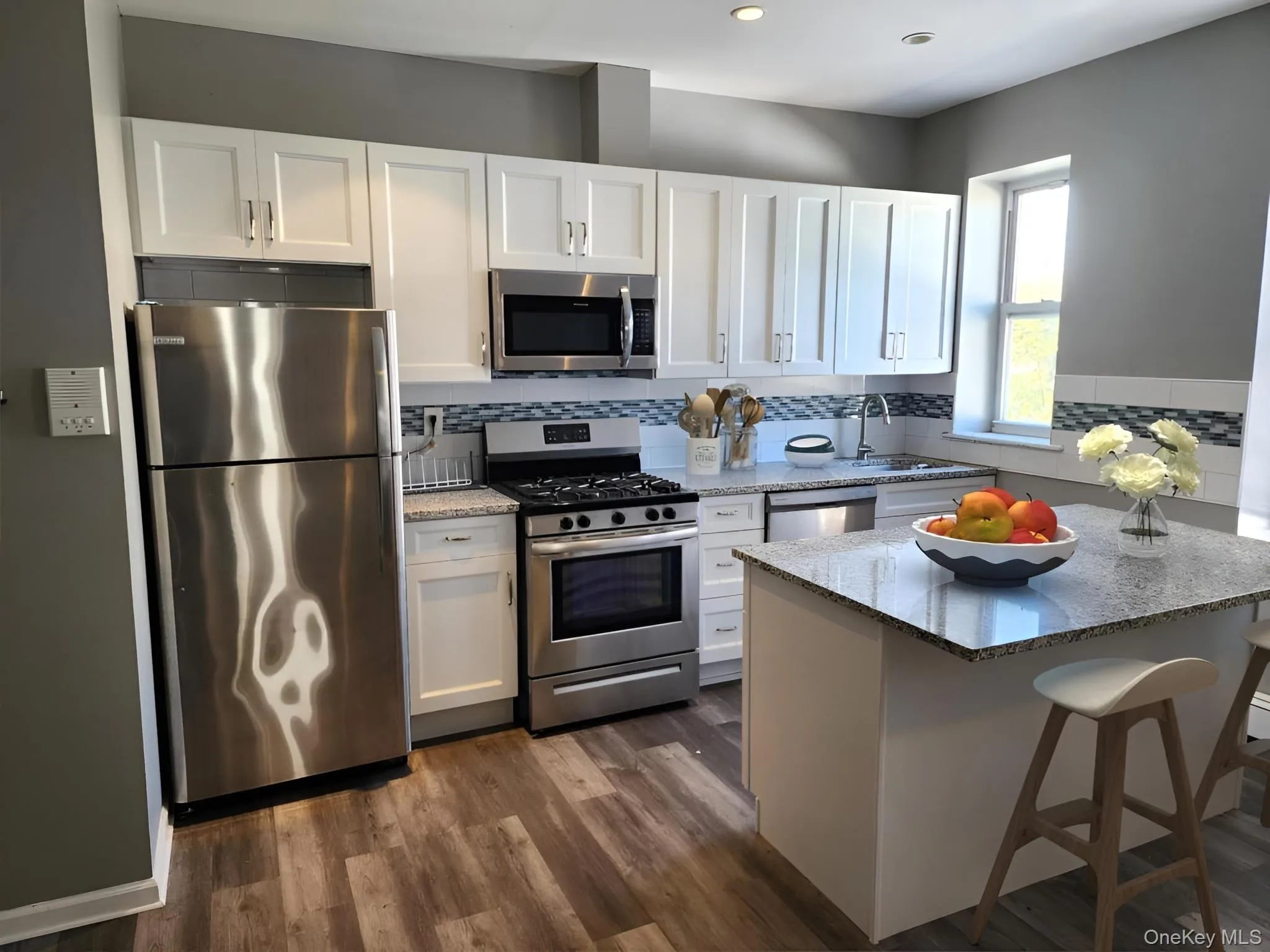 Kitchen featuring white cabinetry, appliances with stainless steel finishes, light stone counters, a breakfast bar area, and decorative backsplash Kitchen featuring white cabinetry, appliances with stainless steel finishes, light stone counters, a breakfast bar area, and decorative backsplash