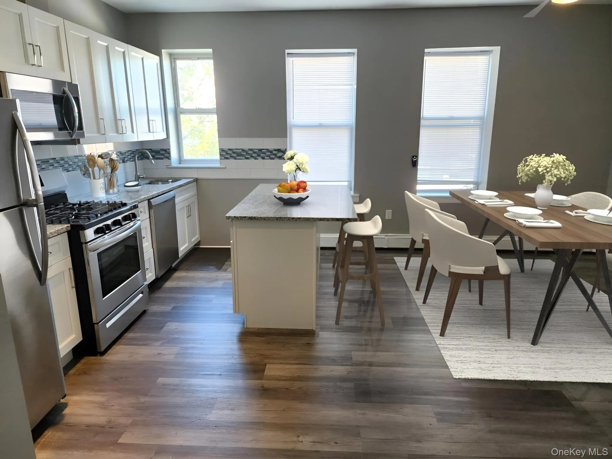 Kitchen featuring white cabinetry, stainless steel appliances, a kitchen island, tasteful backsplash, and dark wood-type flooring Kitchen featuring white cabinetry, stainless steel appliances, a kitchen island, tasteful backsplash, and dark wood-type flooring