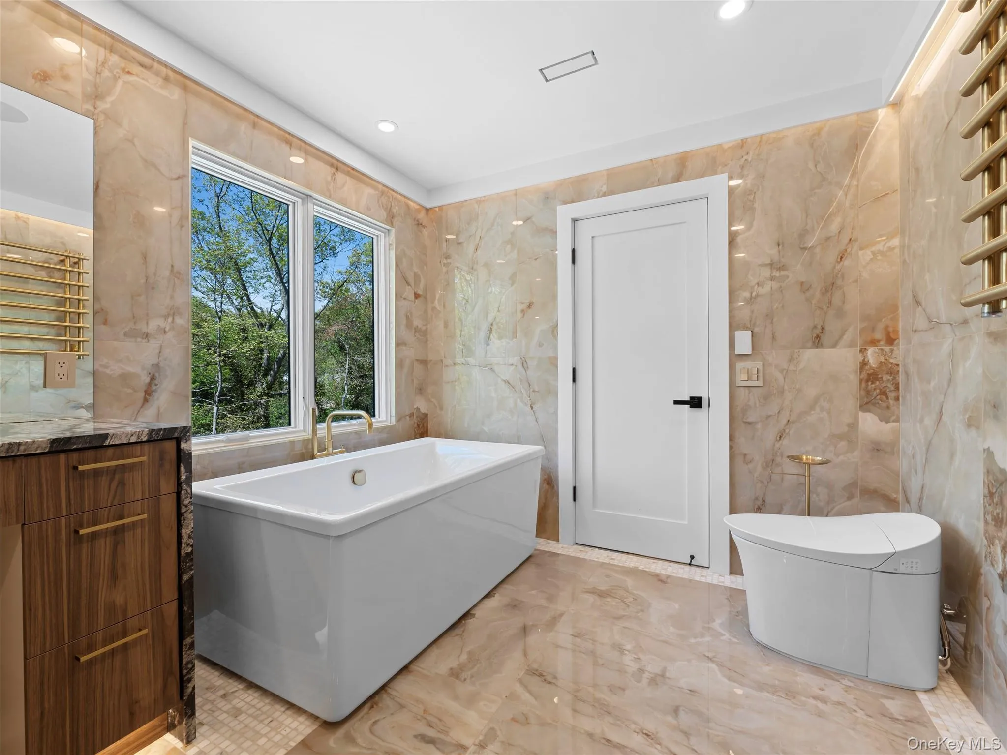 Full bath with a towel warmer, a soaking tub, light marble finish flooring, tile walls, and vanity Full bath with a towel warmer, a soaking tub, light marble finish flooring, tile walls, and vanity