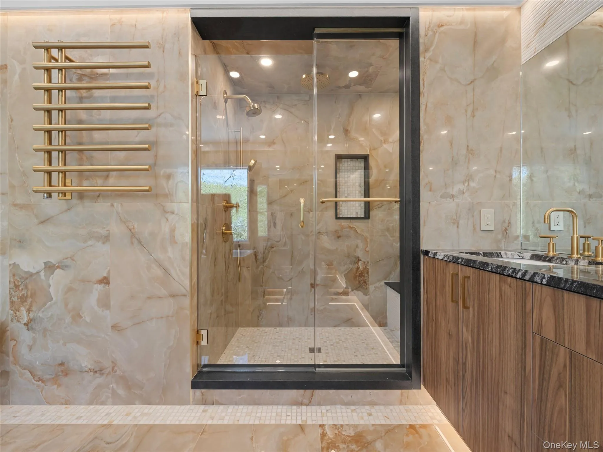 Bathroom with vanity, marble tiled floors, a marble finish shower, tile walls, and a towel warming rack Bathroom with vanity, marble tiled floors, a marble finish shower, tile walls, and a towel warming rack