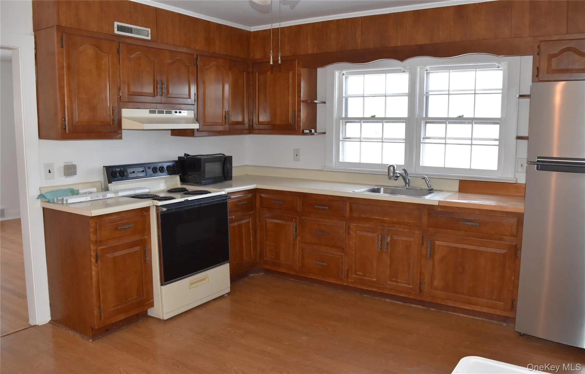 Kitchen with electric range, freestanding refrigerator, brown cabinets, and light countertops Kitchen with electric range, freestanding refrigerator, brown cabinets, and light countertops