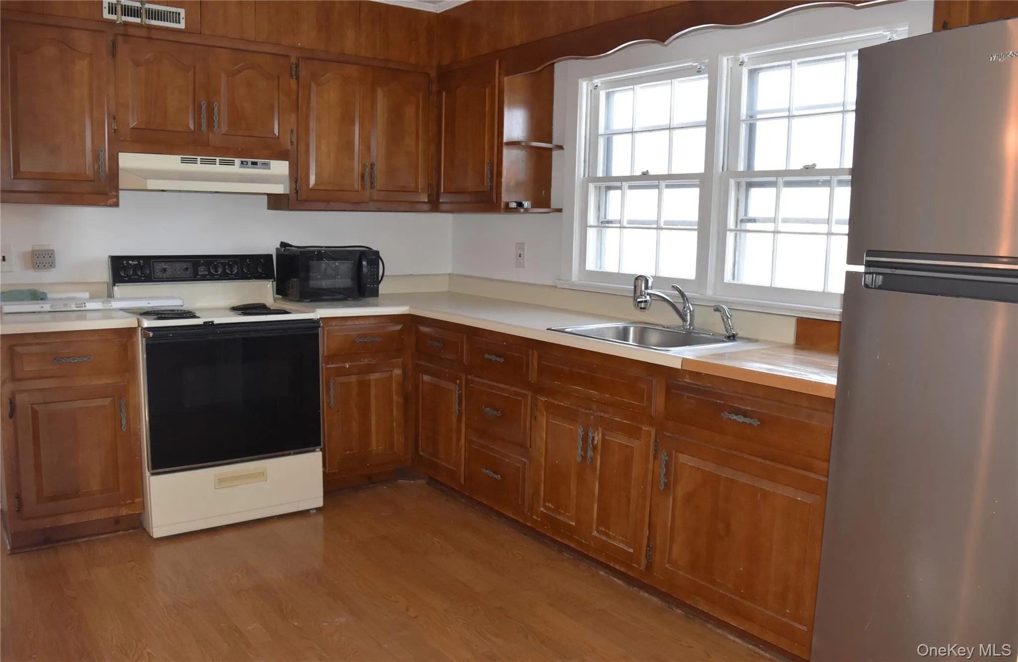 Kitchen with freestanding refrigerator, electric stove, light countertops, and brown cabinetry Kitchen with freestanding refrigerator, electric stove, light countertops, and brown cabinetry