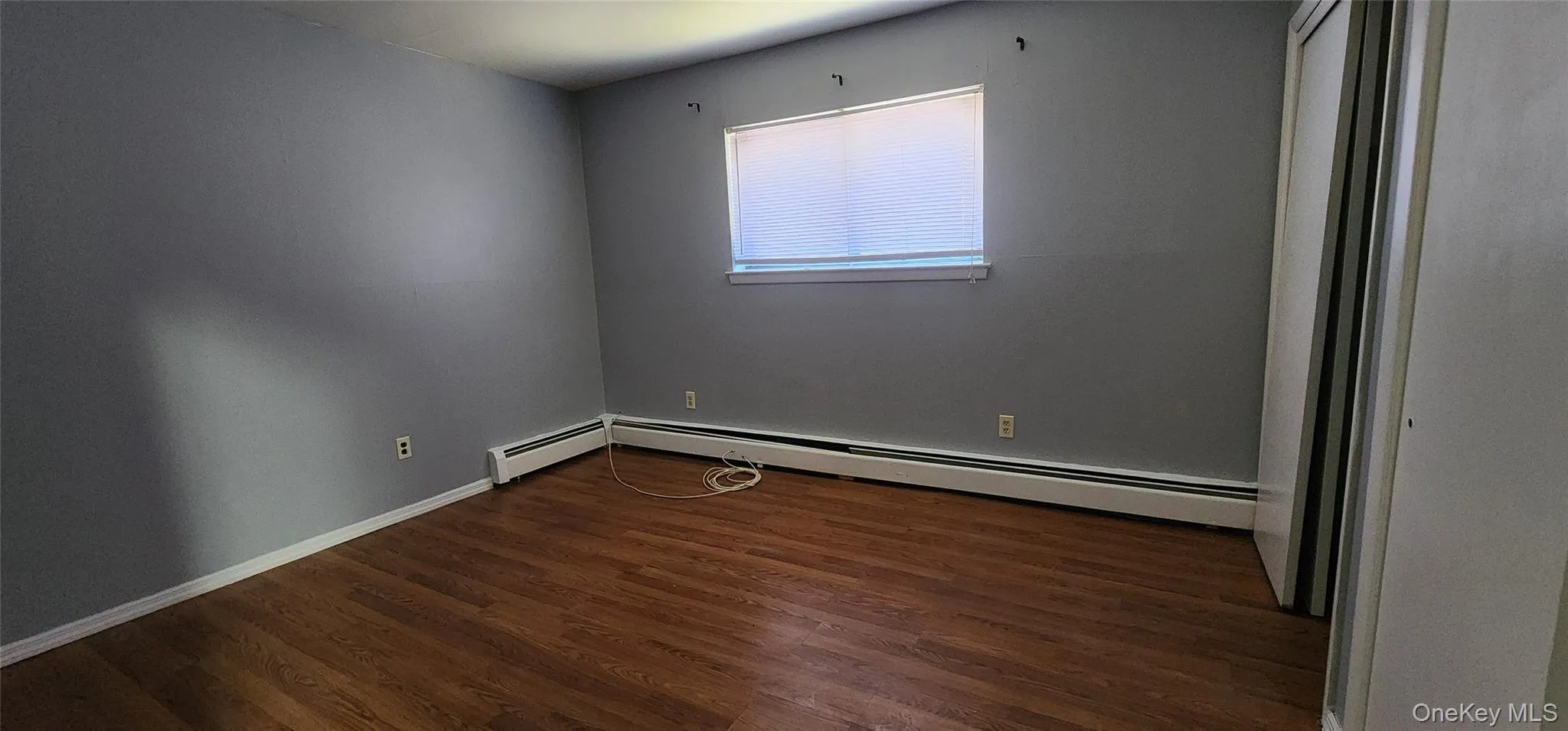 Spare room featuring dark wood-style floors and a baseboard radiator Spare room featuring dark wood-style floors and a baseboard radiator